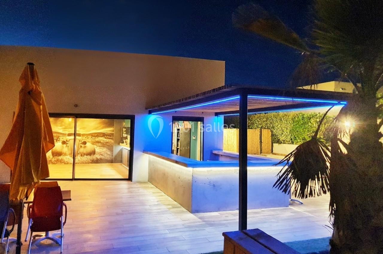 Terrasse moderne éclairée avec piscine, pergola lumineuse et mobilier extérieur, vue de nuit.