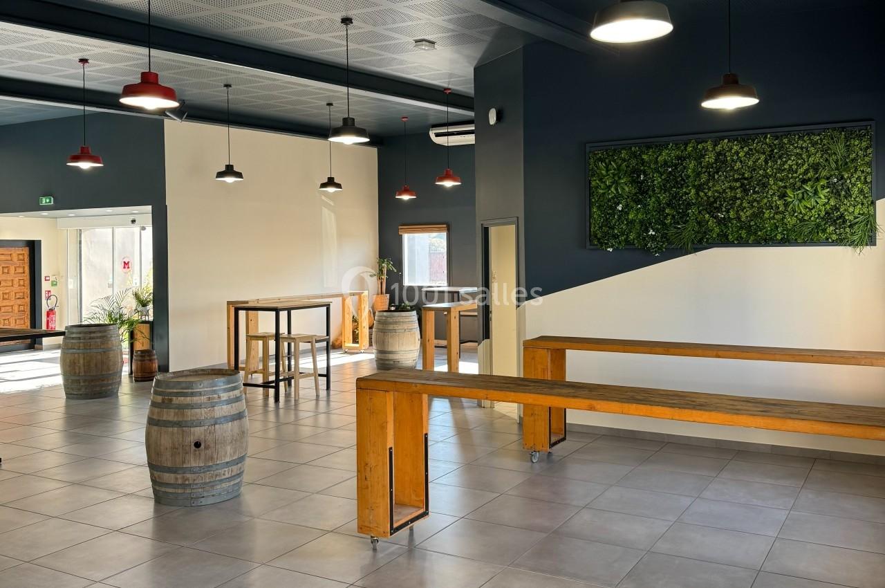 Salle lumineuse avec tables hautes en bois, tonneaux décoratifs, mur végétal et suspensions rouges.