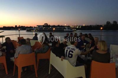 Façade éclairée d'un bâtiment nommé ’Le Yacht’ de nuit, avec des lumières bleues et un espace extérieur aménagé.