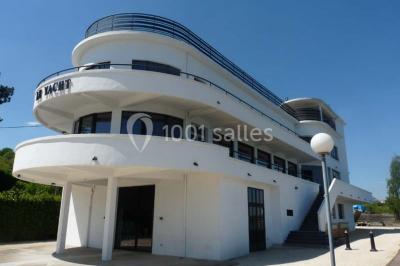 Façade éclairée d'un bâtiment nommé ’Le Yacht’ de nuit, avec des lumières bleues et un espace extérieur aménagé.