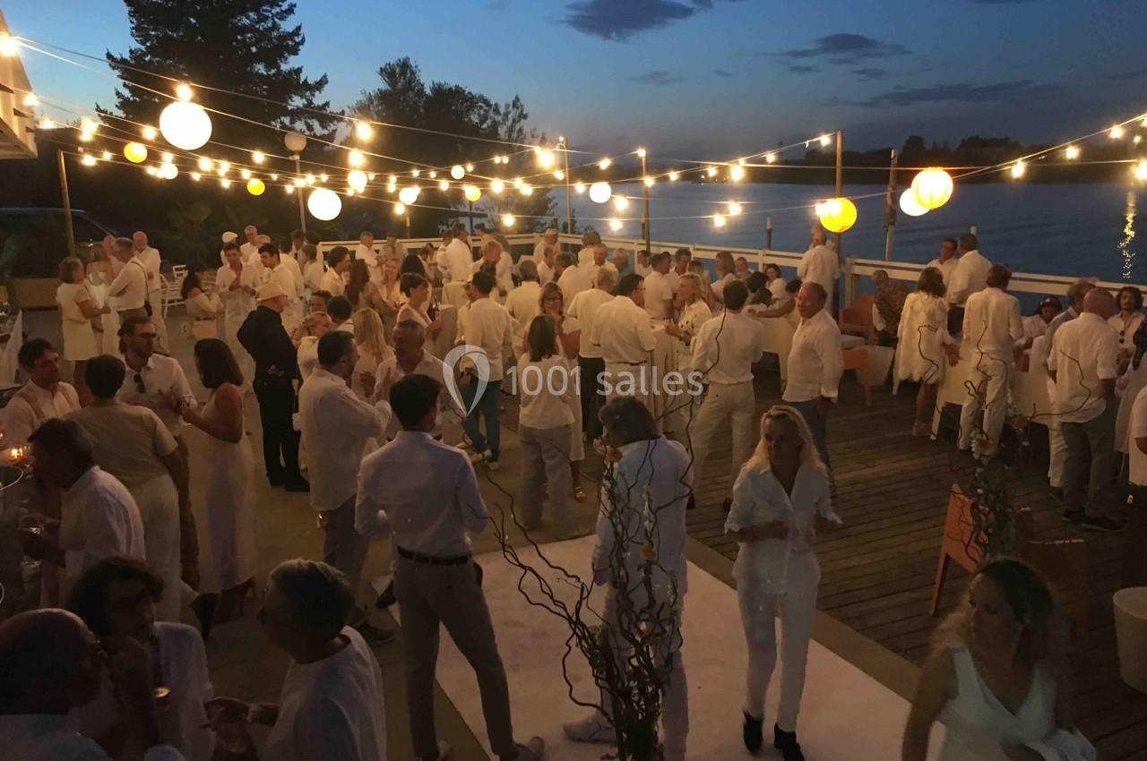 Groupe de personnes en tenue blanche lors d'une soirée en plein air, éclairée par des guirlandes lumineuses, près d'un plan…