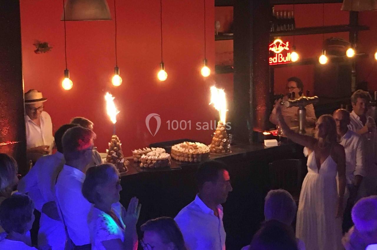 Des invités en tenue blanche célèbrent dans une salle éclairée, avec des desserts décorés de bougies étincelantes.