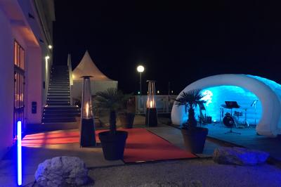 Façade éclairée d'un bâtiment nommé ’Le Yacht’ de nuit, avec des lumières bleues et un espace extérieur aménagé.