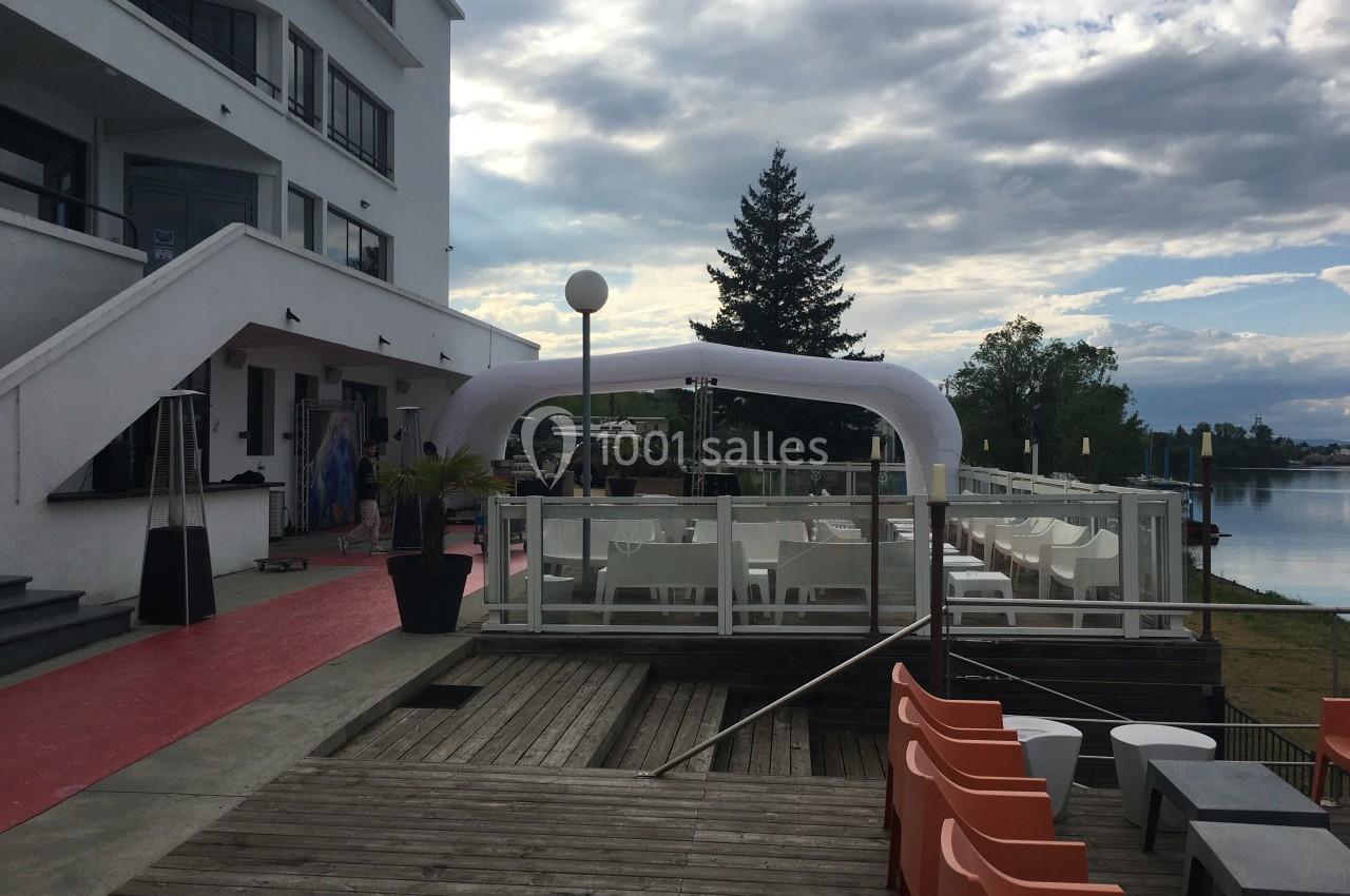 Terrasse extérieure avec mobilier moderne, vue sur un plan d'eau, sous un ciel partiellement nuageux.