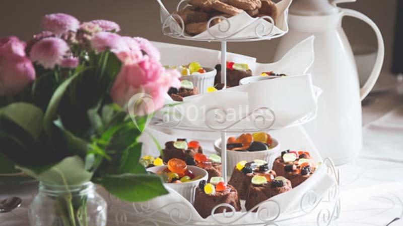 Plateau à étages avec desserts et bonbons, accompagné d'un bouquet de fleurs et d'une carafe blanche en arrière-plan.