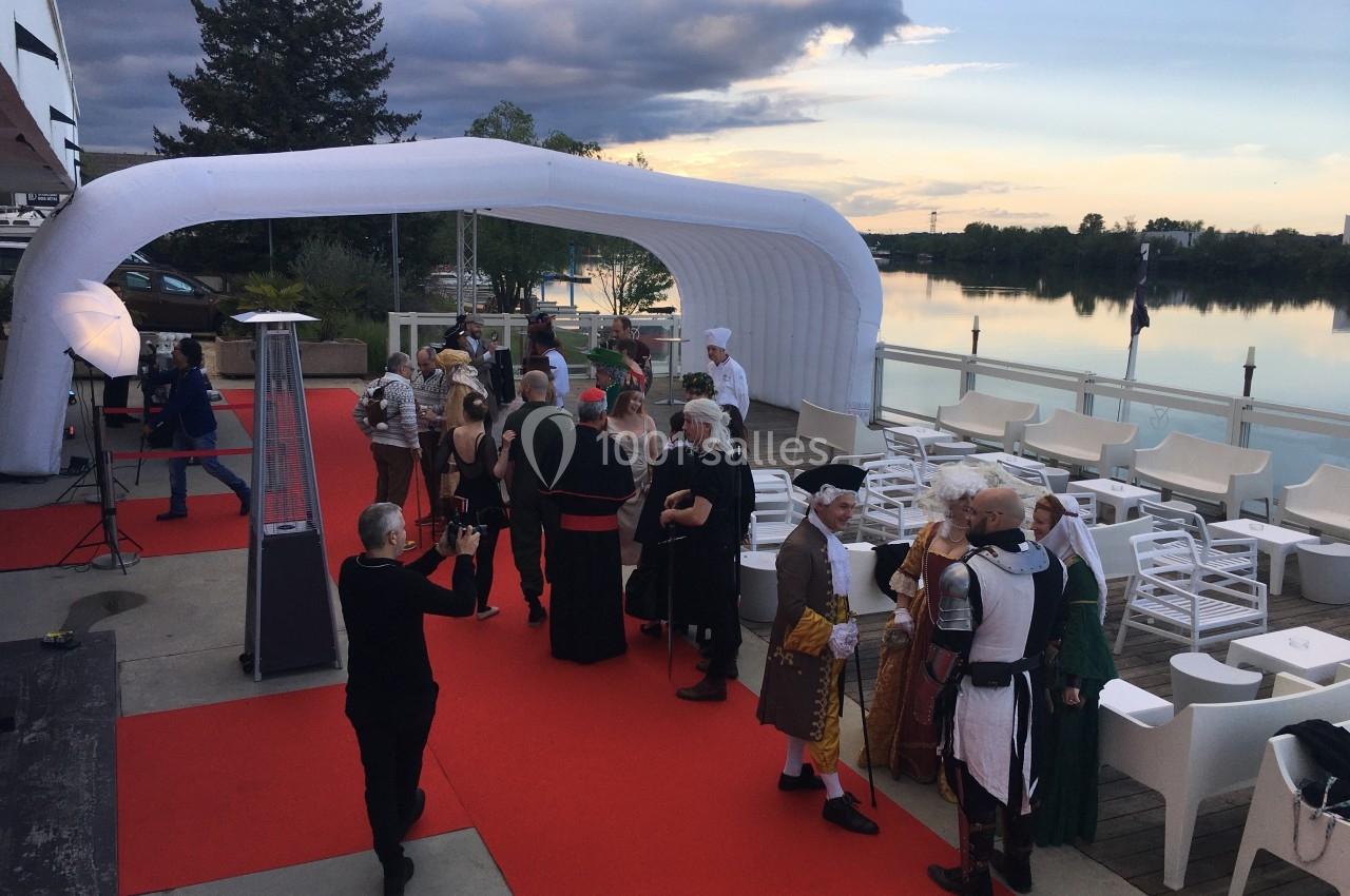Des personnes en costumes médiévaux discutent sur un tapis rouge près d'une terrasse au bord d'un lac.