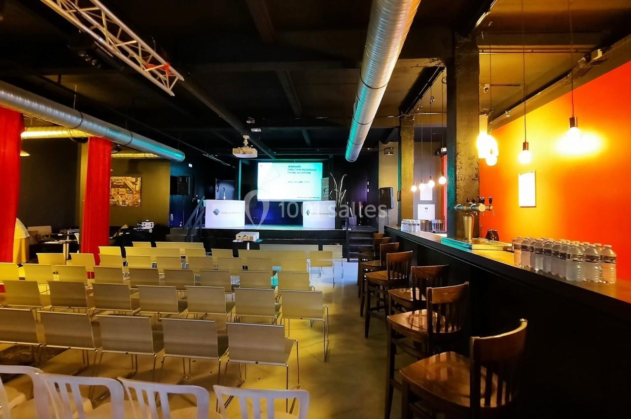 Salle de conférence avec des rangées de chaises vides, un écran de projection allumé et un éclairage chaleureux.