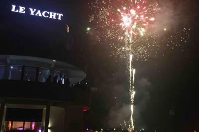 Façade éclairée d'un bâtiment nommé ’Le Yacht’ de nuit, avec des lumières bleues et un espace extérieur aménagé.