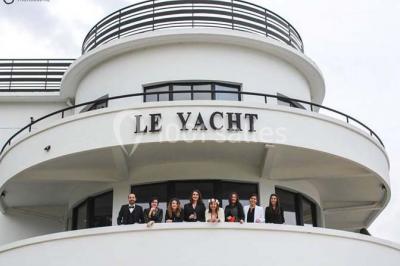 Façade éclairée d'un bâtiment nommé ’Le Yacht’ de nuit, avec des lumières bleues et un espace extérieur aménagé.