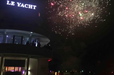 Façade éclairée d'un bâtiment nommé ’Le Yacht’ de nuit, avec des lumières bleues et un espace extérieur aménagé.