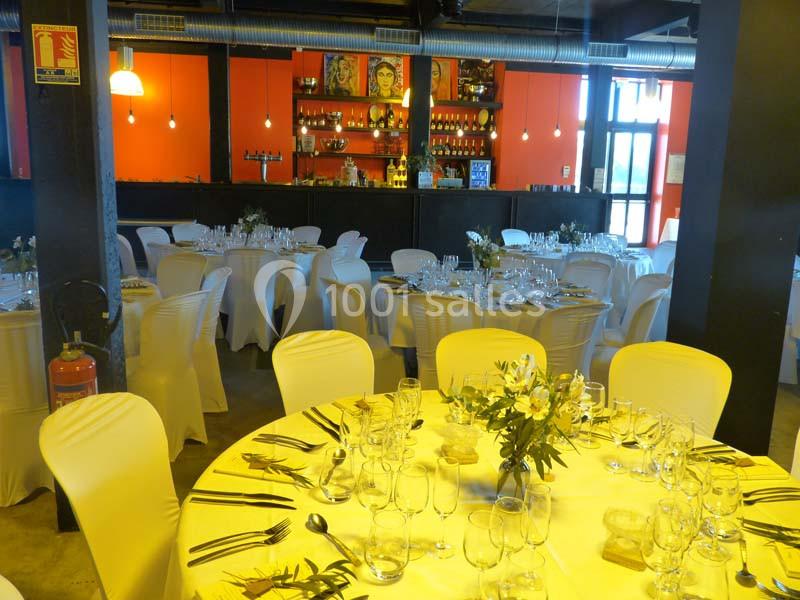 Salle de réception décorée avec des tables rondes dressées, nappes blanches et centre de table floral.