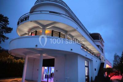 Façade éclairée d'un bâtiment nommé ’Le Yacht’ de nuit, avec des lumières bleues et un espace extérieur aménagé.