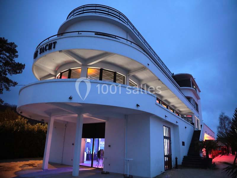 Bâtiment moderne en forme de paquebot avec éclairage intérieur visible à la tombée de la nuit.