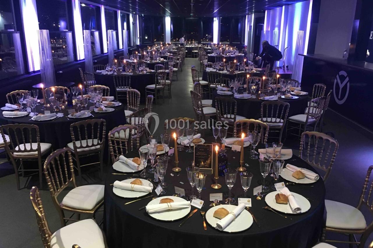 Salle de réception élégamment décorée avec des tables rondes, nappes noires, chandeliers et couverts dressés.