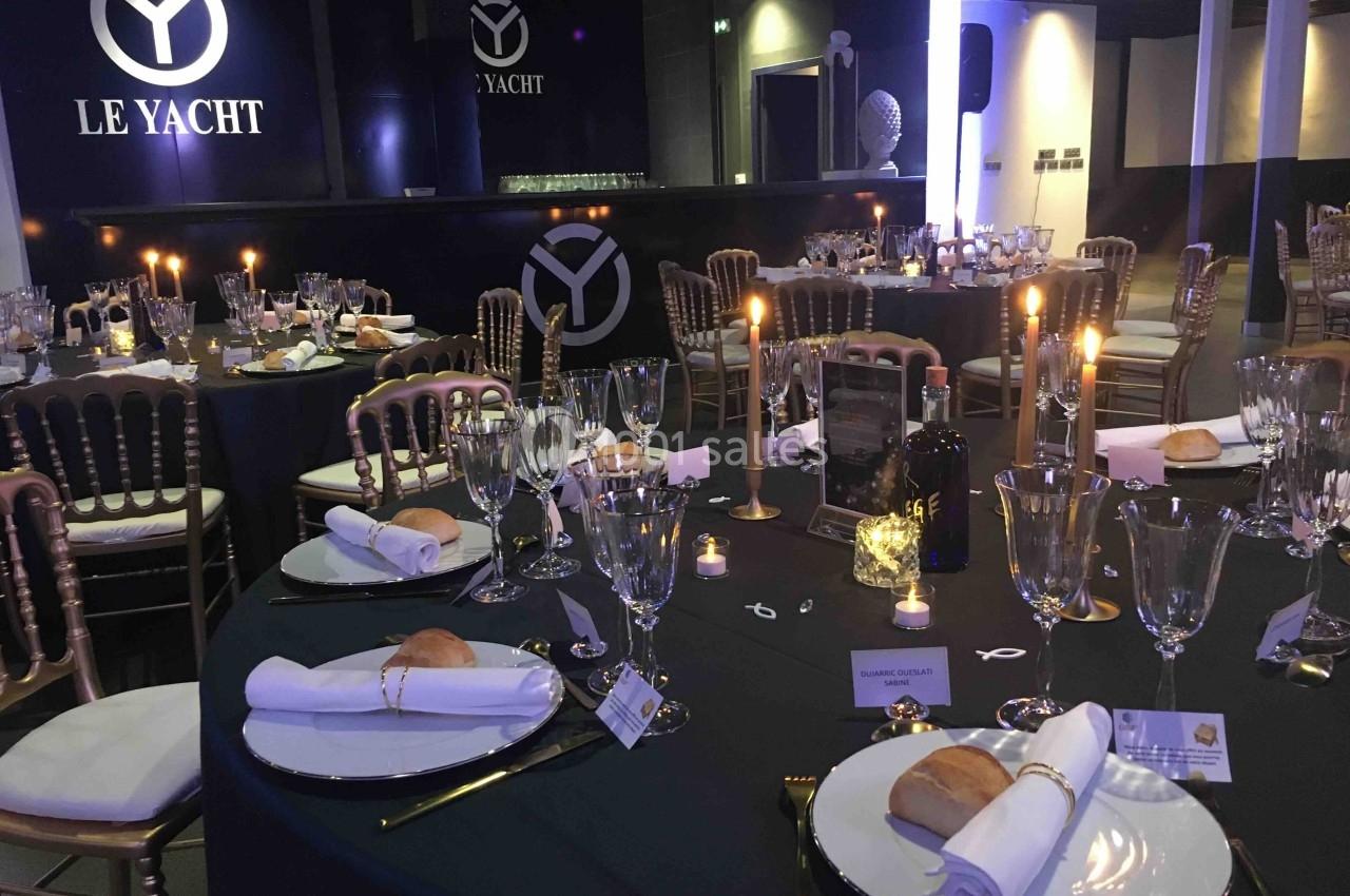 Salle de réception élégamment décorée avec tables dressées, chandelles allumées et vaisselle raffinée.