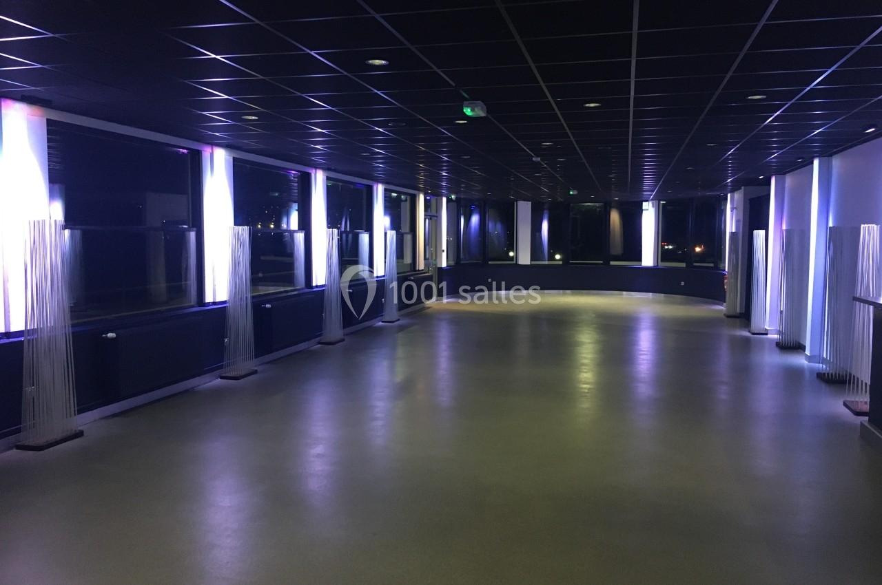 Salle vide avec sol clair, murs sombres et éclairage lumineux diffusé par des colonnes lumineuses modernes.