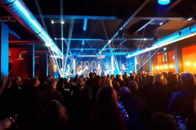 Façade éclairée d'un bâtiment nommé ’Le Yacht’ de nuit, avec des lumières bleues et un espace extérieur aménagé.