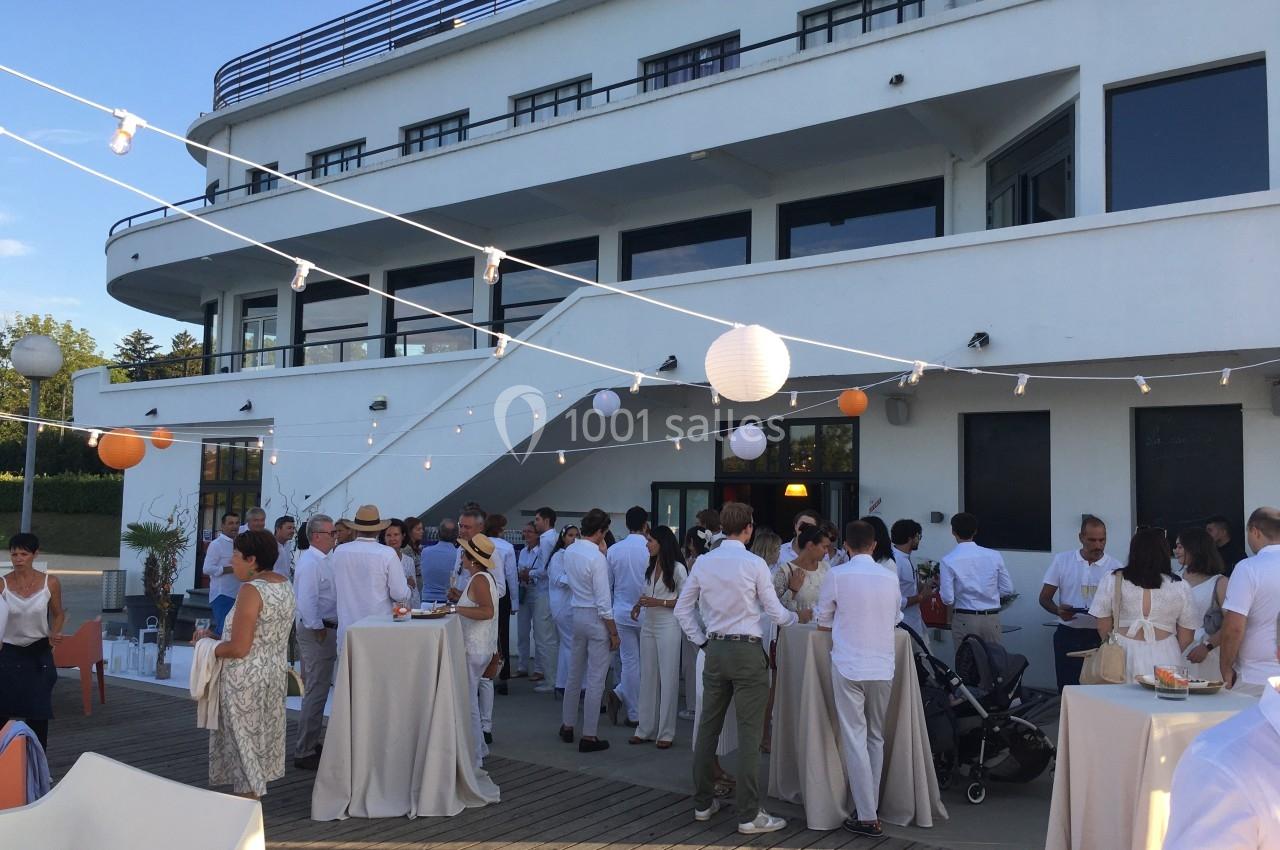 Groupe de personnes en tenue blanche réunies sur une terrasse extérieure, décorée de guirlandes lumineuses et lanternes.
