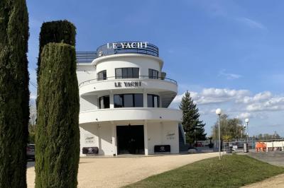 Façade éclairée d'un bâtiment nommé ’Le Yacht’ de nuit, avec des lumières bleues et un espace extérieur aménagé.