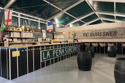 Deux hommes en tenue de rugby bleue simulent une action de jeu dans une salle éclairée avec des chaises vides.