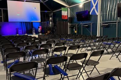 Deux hommes en tenue de rugby bleue simulent une action de jeu dans une salle éclairée avec des chaises vides.