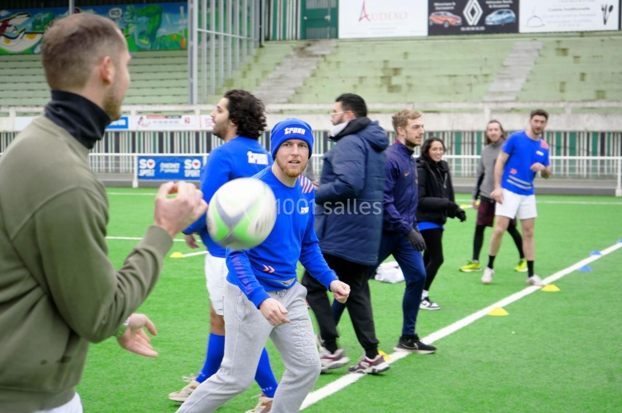 Des personnes participent à un entraînement de rugby sur un terrain en plein air, certaines en mouvement.