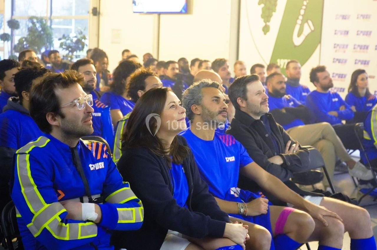 Un groupe de personnes assises, attentives à une présentation dans une salle lumineuse, portant des vêtements bleus.