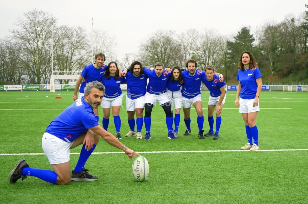 Un groupe de joueurs et joueuses de rugby en tenue bleue posant sur un terrain gazonné.