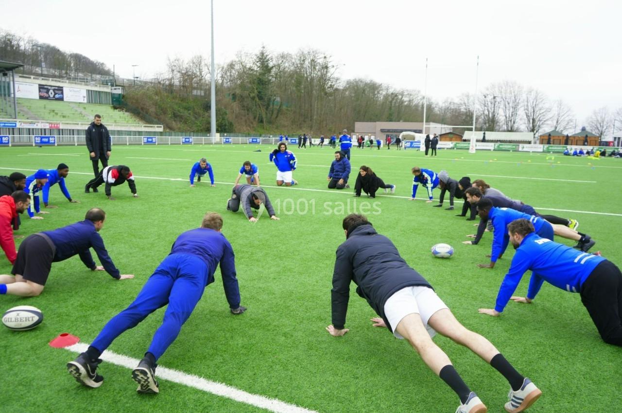 Des joueurs de rugby s'échauffent en faisant des pompes sur un terrain en plein air.