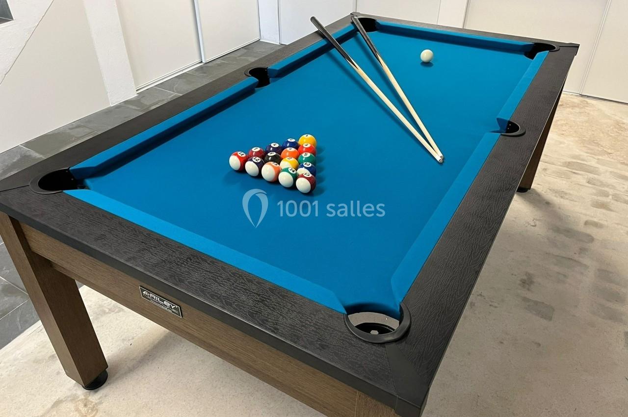 Table de billard avec tapis bleu, deux queues posées dessus et les boules alignées en triangle.
