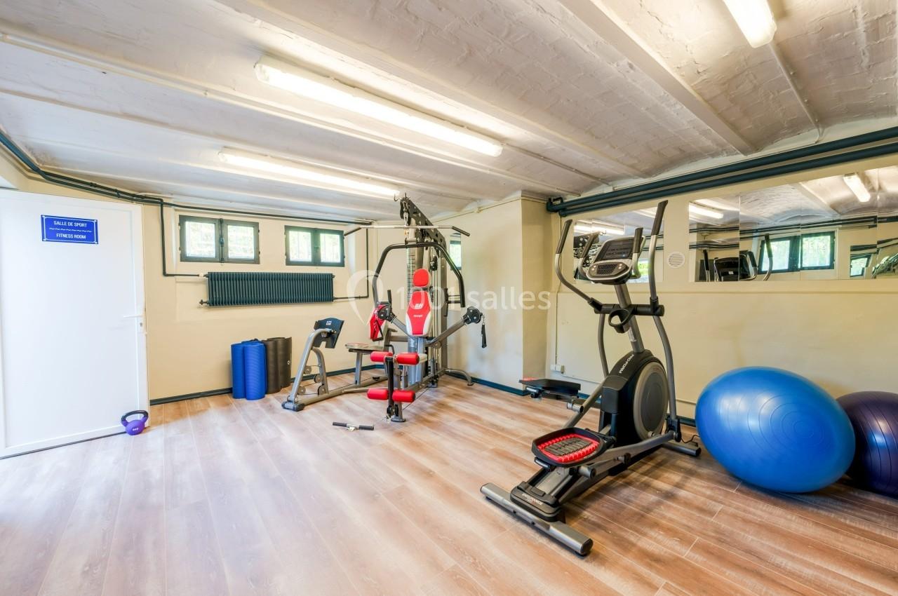 Salle de sport lumineuse avec équipements de musculation, vélo elliptique, ballons d'exercice et miroirs muraux.