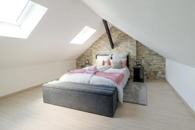 Chambre lumineuse avec lit double, fauteuils blancs, tapis coloré et mobilier en bois sous un plafond avec poutres…