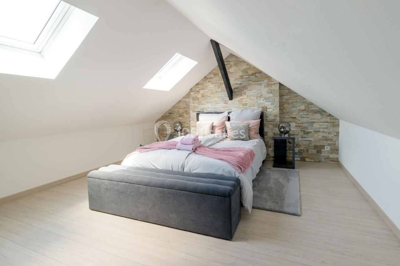 Chambre mansardée avec lit double, mur en pierre, lumière naturelle provenant de deux fenêtres de toit.