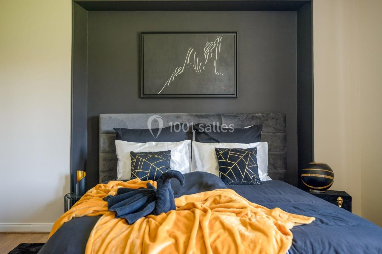 Lit double avec linge de lit noir et jaune, décoré de coussins géométriques et d'un tableau abstrait au mur.