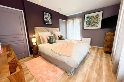 Chambre lumineuse avec lit double, fauteuils blancs, tapis coloré et mobilier en bois sous un plafond avec poutres…