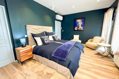 Chambre lumineuse avec lit double, fauteuils blancs, tapis coloré et mobilier en bois sous un plafond avec poutres…