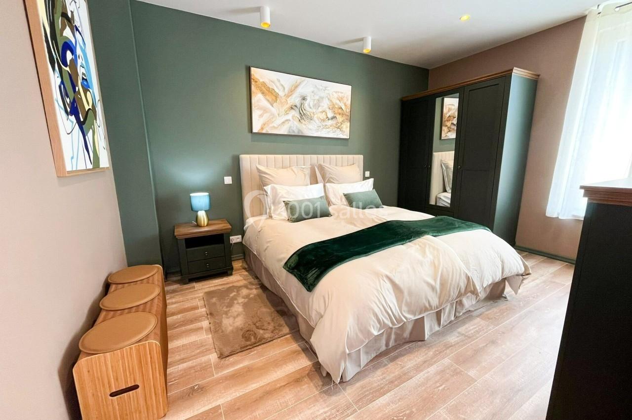 Chambre moderne avec lit double, mur vert, tableaux décoratifs, parquet clair et armoire sombre.