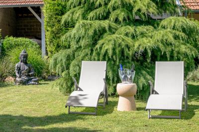 Chambre lumineuse avec lit double, fauteuils blancs, tapis coloré et mobilier en bois sous un plafond avec poutres…