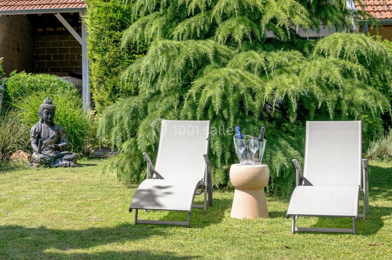 Deux chaises longues sur une pelouse, avec une table basse portant un seau à champagne, près d'une statue de Bouddha.