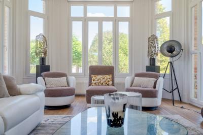 Chambre lumineuse avec lit double, fauteuils blancs, tapis coloré et mobilier en bois sous un plafond avec poutres…