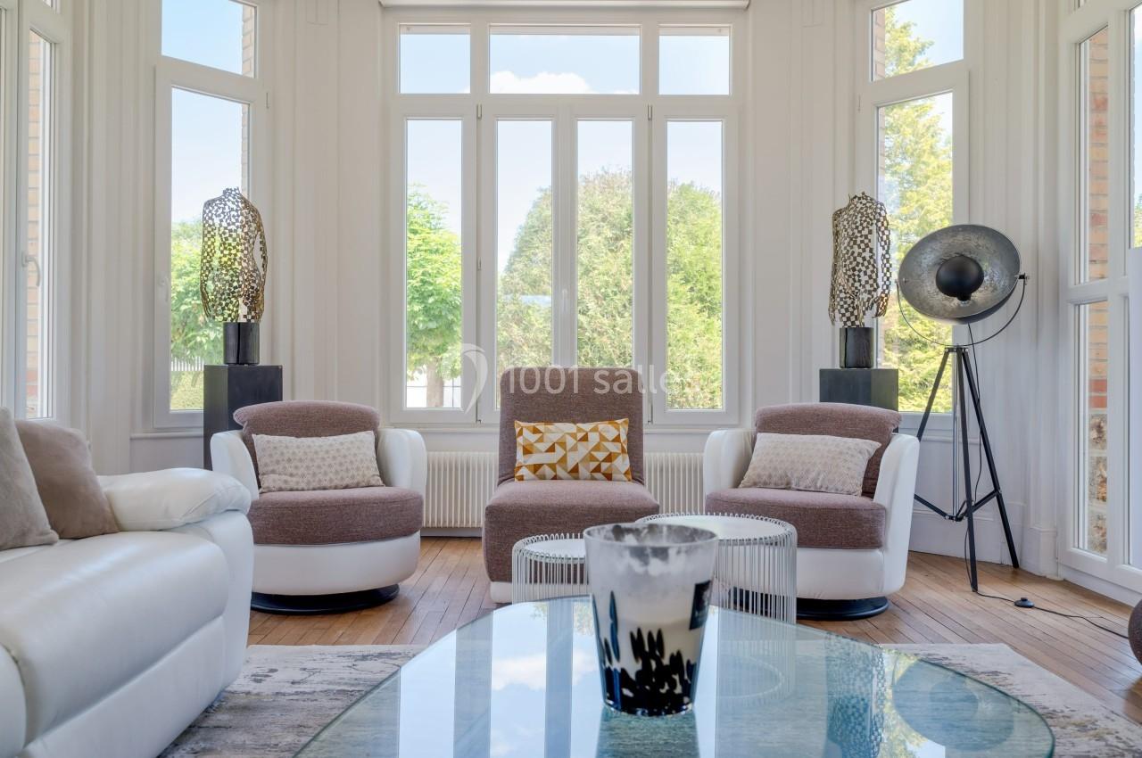 Salon lumineux avec fauteuils modernes, grandes fenêtres donnant sur un jardin et décoration contemporaine.