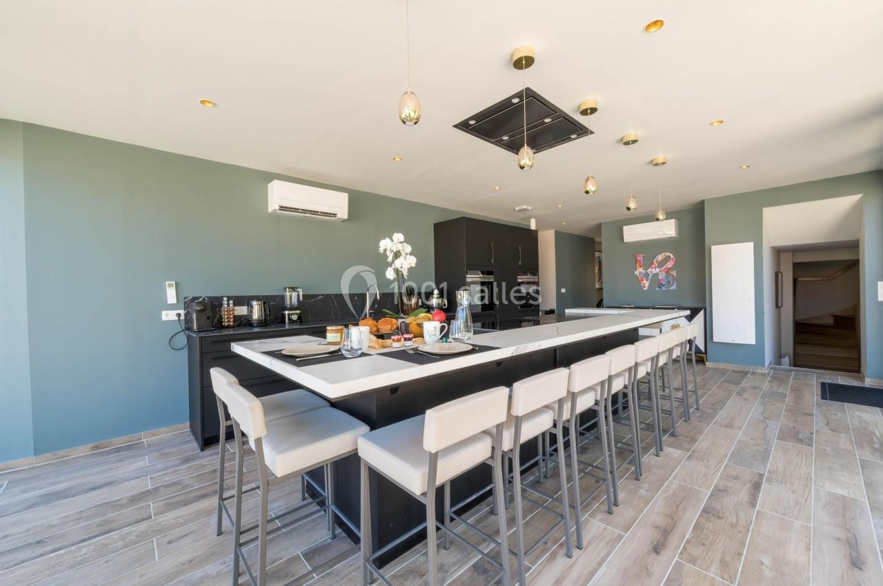 Cuisine moderne avec un grand îlot central, chaises hautes, plan de travail noir et éclairage suspendu.