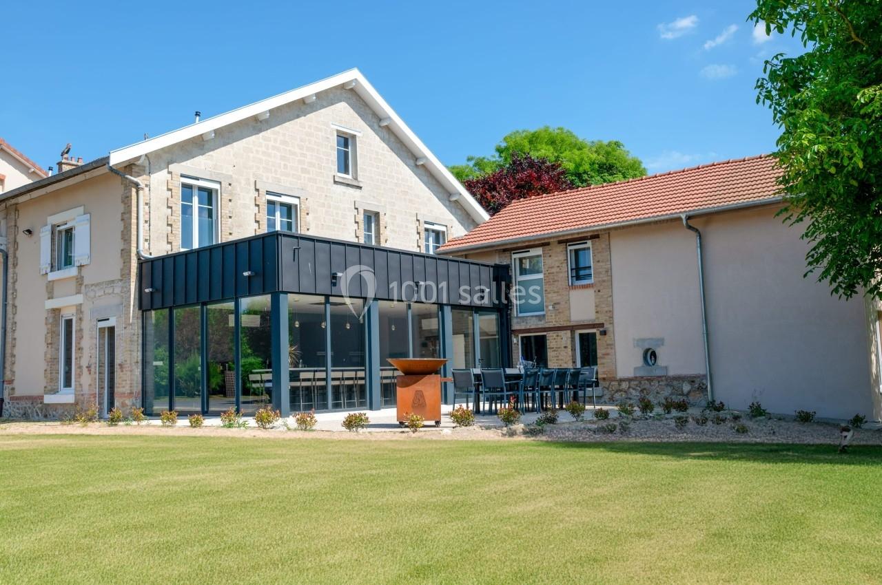 Façade d'une maison rénovée avec une extension moderne en verre et métal, entourée d'un jardin bien entretenu.