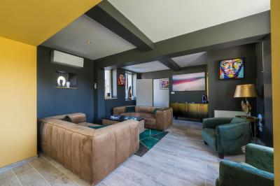 Chambre lumineuse avec lit double, fauteuils blancs, tapis coloré et mobilier en bois sous un plafond avec poutres…