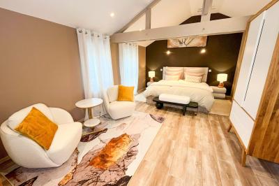 Chambre lumineuse avec lit double, fauteuils blancs, tapis coloré et mobilier en bois sous un plafond avec poutres…