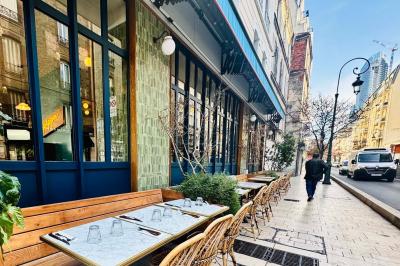 Terrasse de café avec tables en marbre et chaises en osier, située le long d'une rue pavée bordée de bâtiments urbains.