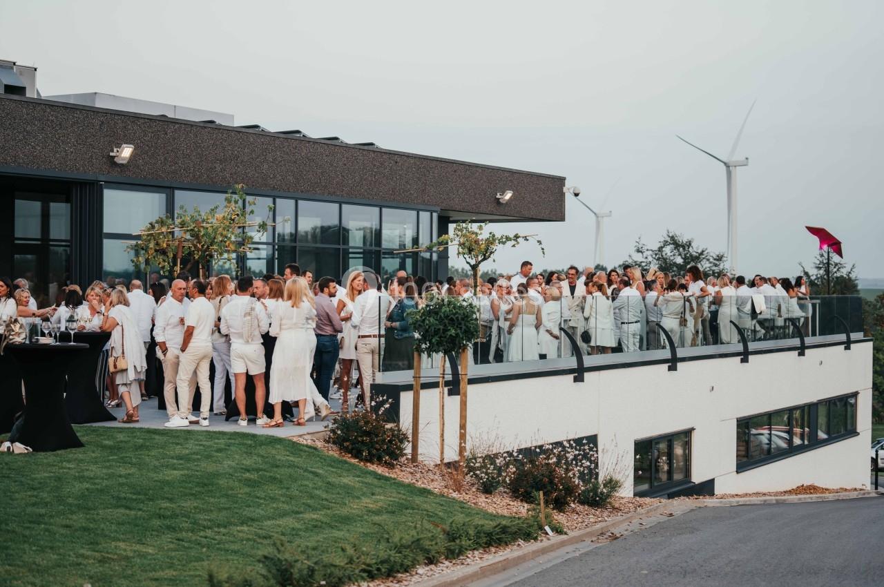 Groupe de personnes en tenue blanche rassemblées sur une terrasse moderne lors d'un événement en extérieur.