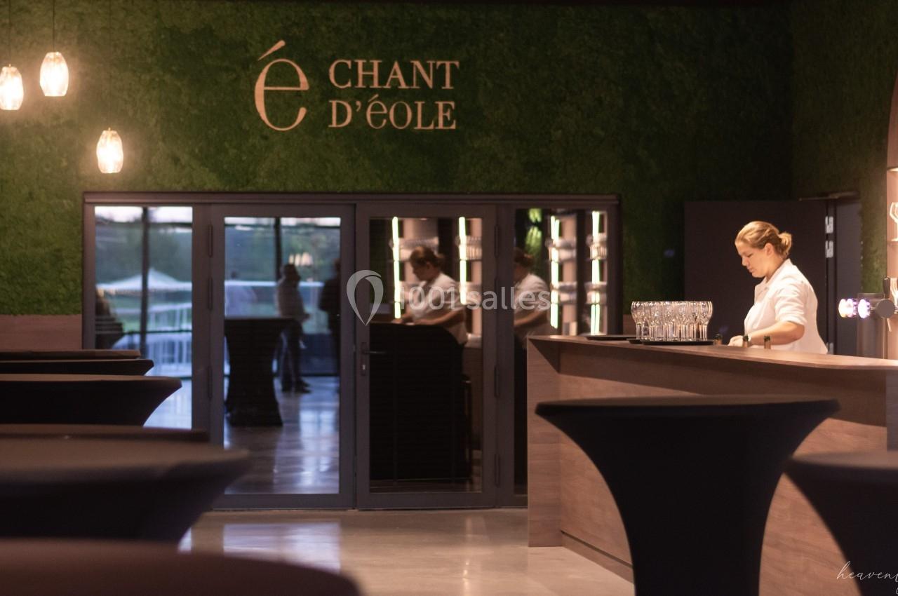 Serveuse préparant des verres au comptoir d'un bar élégant, décoré de murs verts et éclairé par une lumière douce.