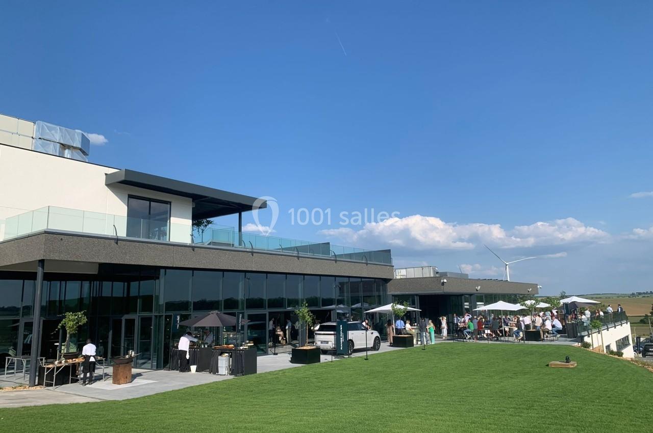 Terrasse moderne avec tables et parasols, entourée de verdure, sous un ciel bleu dégagé.