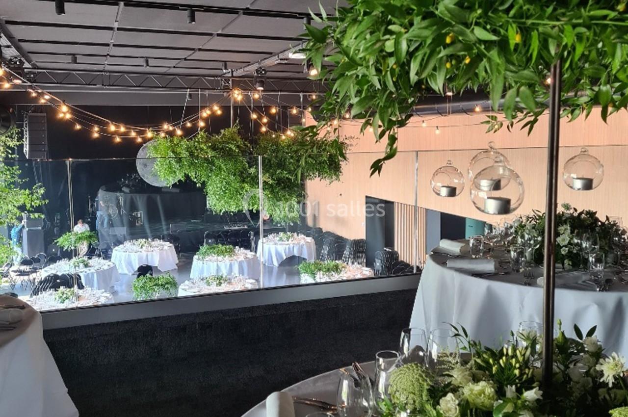 Salle de réception décorée avec des tables dressées, des guirlandes lumineuses et des arrangements floraux.